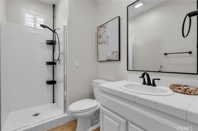 bathroom with a tile shower, wood finished floors, toilet, and vanity