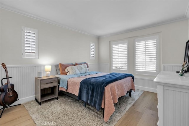 bedroom featuring a wainscoted wall, light wood-style floors, and crown molding