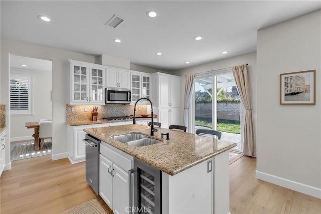 kitchen featuring white cabinetry, stainless steel appliances, a sink, beverage cooler, and visible vents