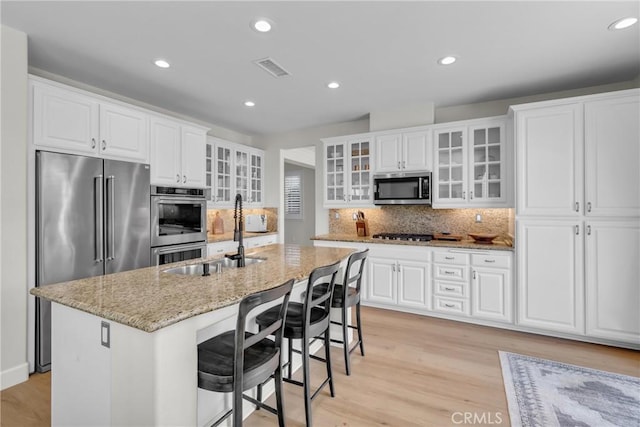kitchen featuring decorative backsplash, light stone countertops, appliances with stainless steel finishes, a sink, and light wood-type flooring