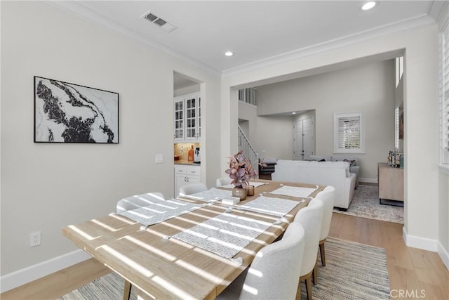 dining space with light wood-style flooring, visible vents, crown molding, baseboards, and stairs