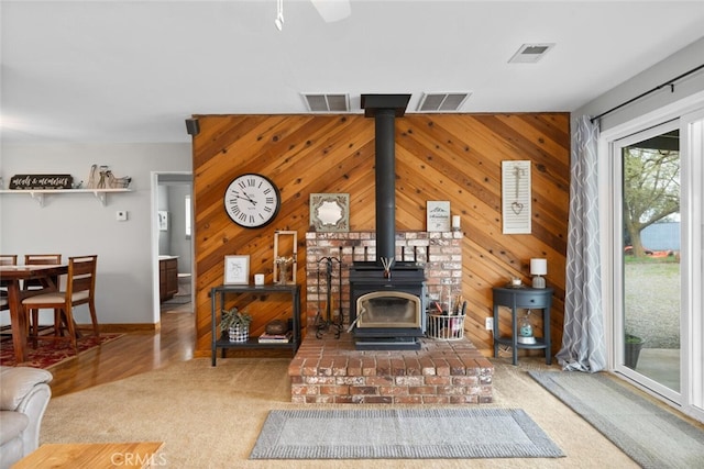carpeted living area featuring wooden walls, a wood stove, and visible vents