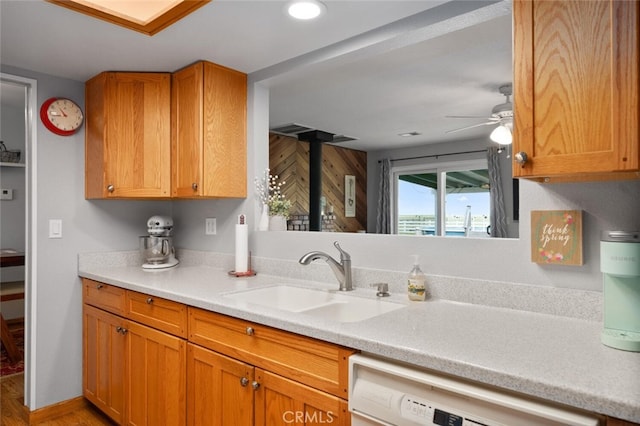 kitchen featuring light countertops, a sink, dishwasher, a ceiling fan, and brown cabinetry