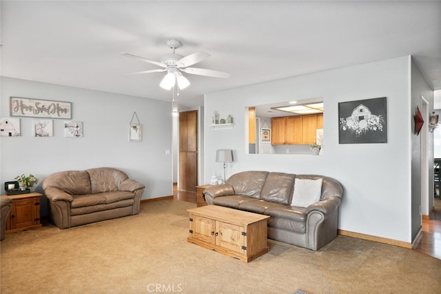 living area featuring baseboards, ceiling fan, and light colored carpet