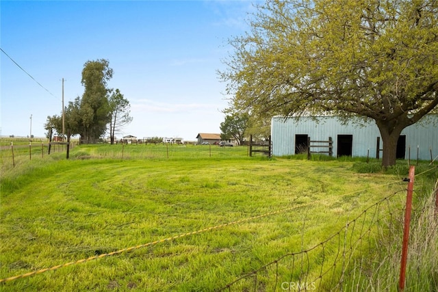 view of yard with an outdoor structure, a pole building, fence, and a rural view