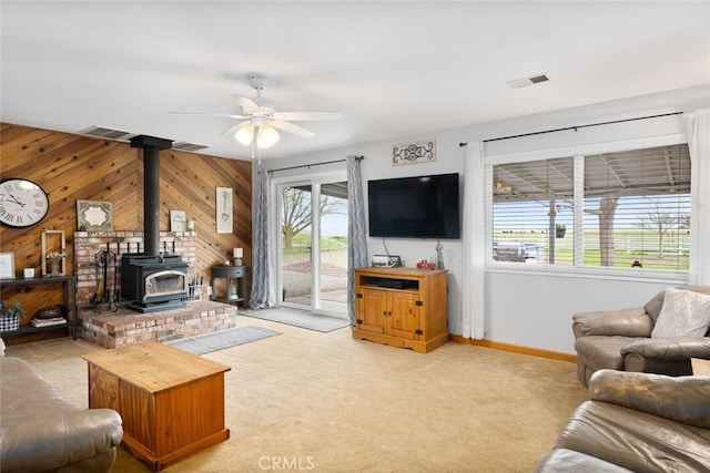 living area with ceiling fan, a wood stove, light colored carpet, and visible vents