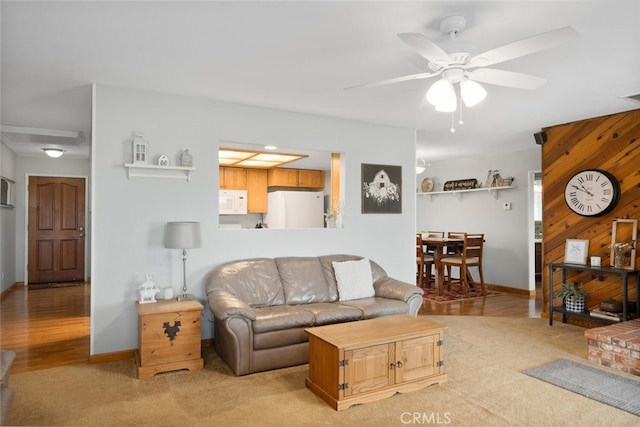 living room featuring light carpet, baseboards, wooden walls, and ceiling fan