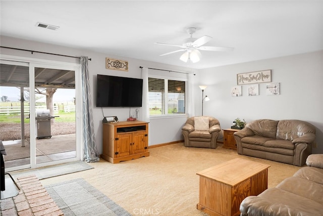 living room featuring baseboards, visible vents, a ceiling fan, and light colored carpet