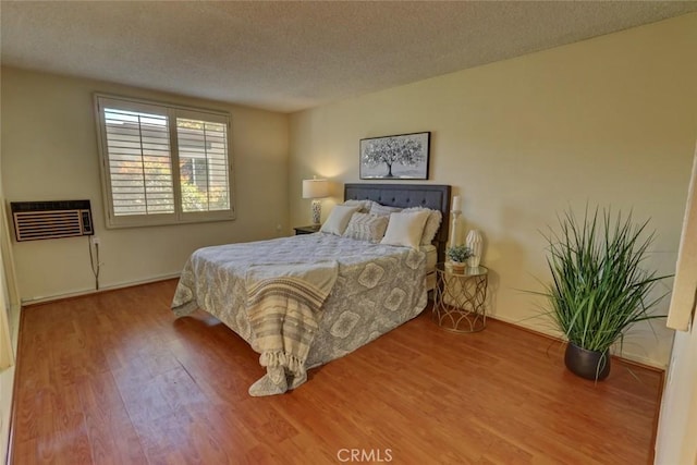 bedroom with an AC wall unit, wood finished floors, and a textured ceiling