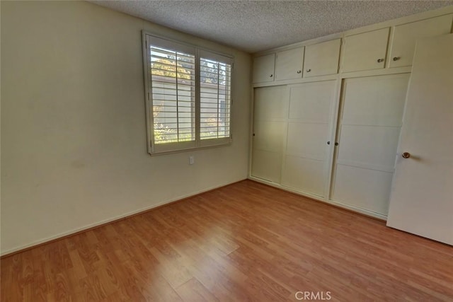 unfurnished bedroom featuring light wood-type flooring, a closet, and a textured ceiling