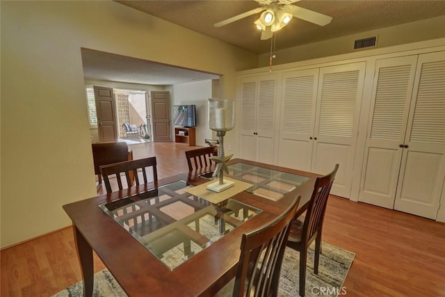dining area featuring visible vents, light wood-style flooring, a textured ceiling, and ceiling fan