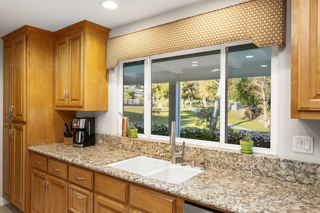 kitchen with recessed lighting, light stone counters, brown cabinetry, and a sink