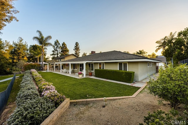 back of property at dusk featuring a yard, a patio, fence, and a chimney