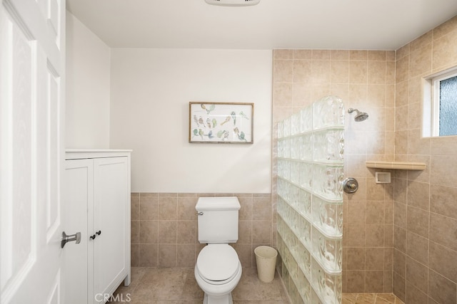 bathroom with a walk in shower, toilet, tile walls, and a wainscoted wall