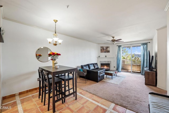 dining area featuring a high end fireplace, crown molding, baseboards, light colored carpet, and ceiling fan with notable chandelier