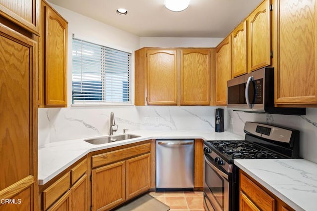 kitchen with light tile patterned floors, decorative backsplash, light stone counters, appliances with stainless steel finishes, and a sink