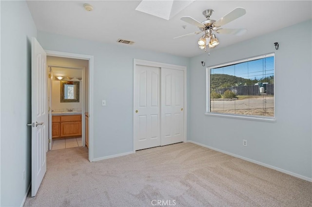 unfurnished bedroom with a closet, light carpet, a skylight, baseboards, and visible vents