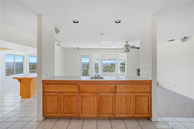 kitchen featuring tile countertops, a healthy amount of sunlight, brown cabinetry, and a ceiling fan