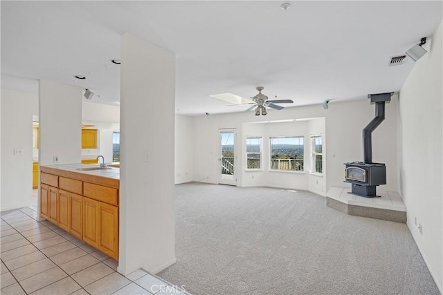 living area featuring a wood stove, light tile patterned flooring, visible vents, light carpet, and ceiling fan