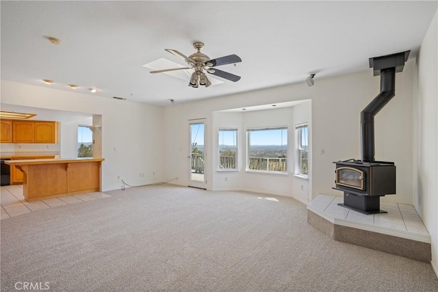 unfurnished living room featuring a wood stove, baseboards, visible vents, light carpet, and ceiling fan