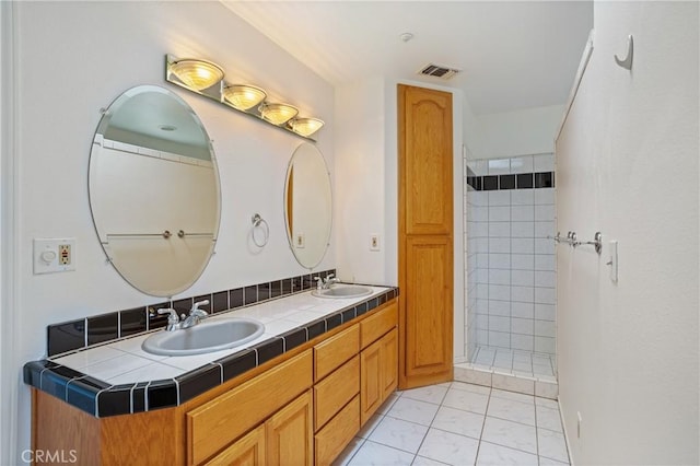 bathroom with visible vents, a sink, double vanity, and tiled shower