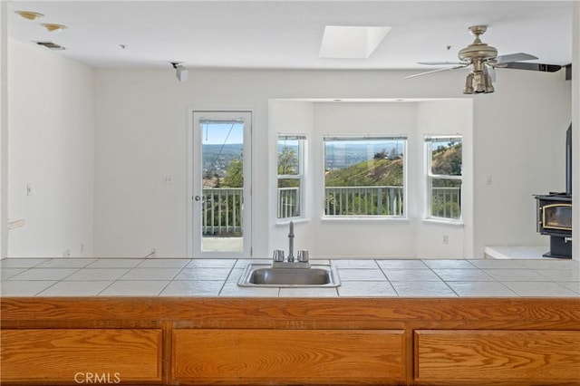 kitchen featuring a wood stove, tile patterned floors, a sink, tile countertops, and ceiling fan