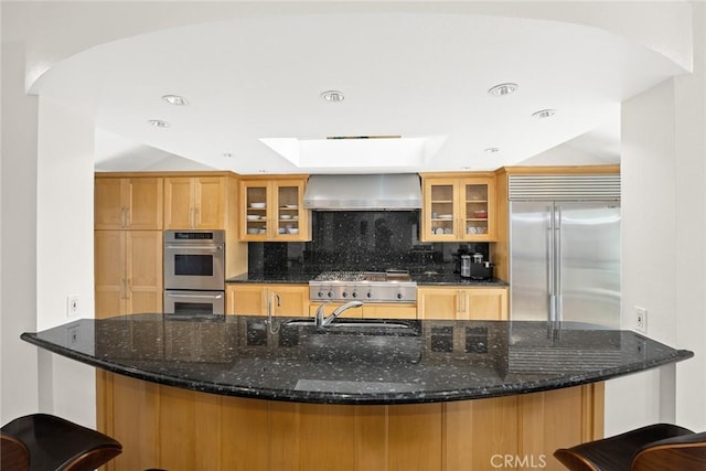 16449 Ladona Cir, Huntington Beach, CA 92649 - kitchen featuring appliances with stainless steel finishes, wall chimney range hood, backsplash, a skylight, and dark stone counters