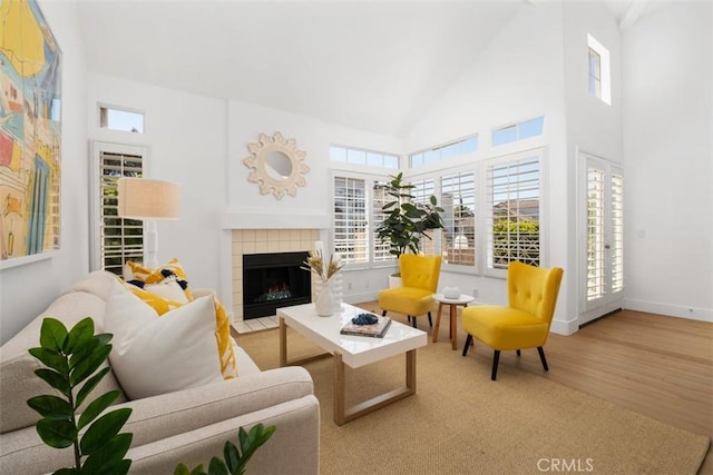 living area featuring high vaulted ceiling, wood finished floors, baseboards, and a tile fireplace