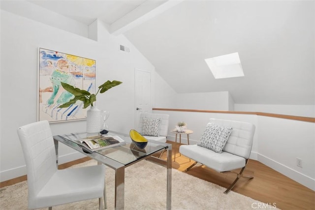home office with lofted ceiling with skylight, wood finished floors, baseboards, and visible vents