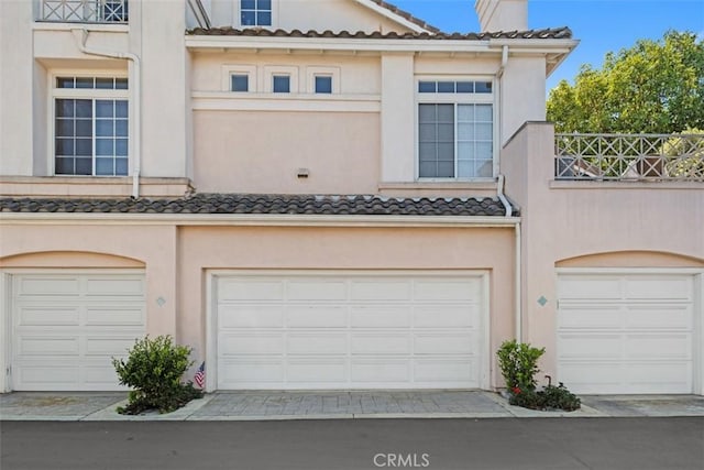 view of front facade featuring stucco siding, a tiled roof, and a garage