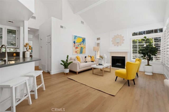 living area featuring visible vents, a fireplace, high vaulted ceiling, and light wood-type flooring