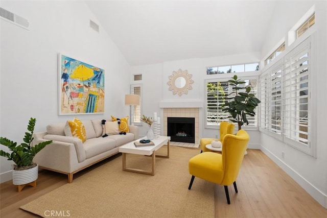 living room featuring wood finished floors, baseboards, visible vents, high vaulted ceiling, and a fireplace