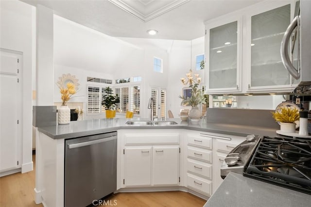 kitchen with light wood-style flooring, appliances with stainless steel finishes, a peninsula, white cabinetry, and a sink
