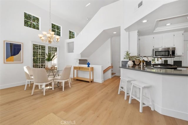 dining area featuring baseboards, light wood-type flooring, recessed lighting, a notable chandelier, and high vaulted ceiling