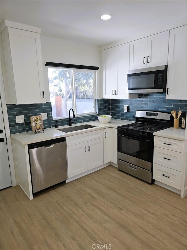kitchen featuring light wood finished floors, a sink, white cabinetry, stainless steel appliances, and light countertops
