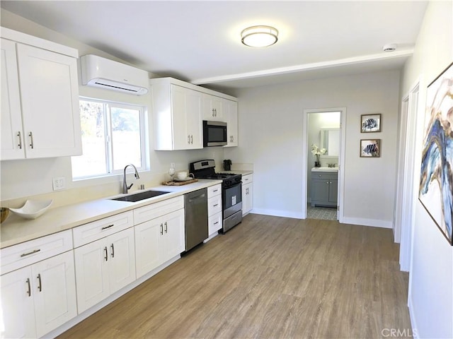 kitchen with stainless steel appliances, a sink, an AC wall unit, white cabinets, and light wood-type flooring