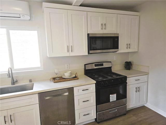 kitchen featuring an AC wall unit, light countertops, appliances with stainless steel finishes, white cabinetry, and a sink