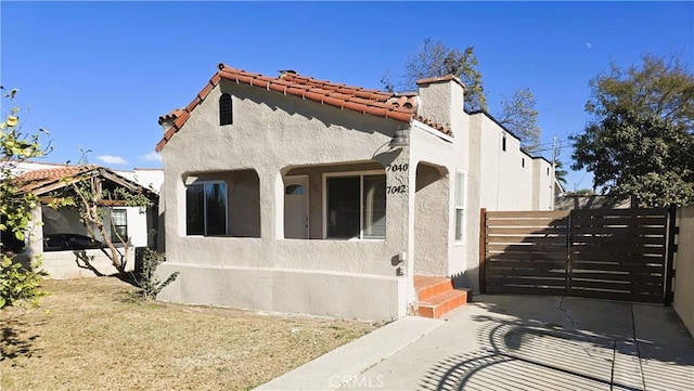 mediterranean / spanish home with a tile roof, stucco siding, a chimney, and fence