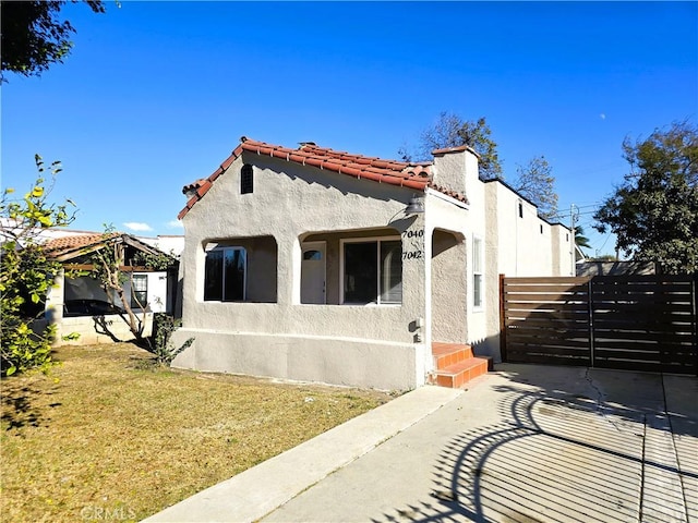 view of front facade featuring a front yard, a tiled roof, fence, and stucco siding