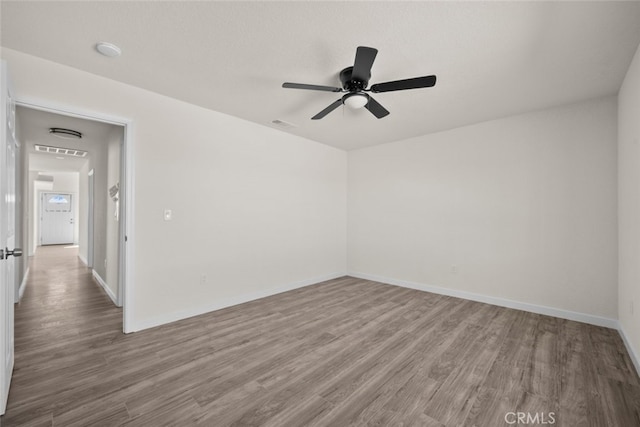 empty room with visible vents, a ceiling fan, baseboards, and wood finished floors