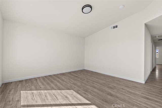 unfurnished room featuring vaulted ceiling, visible vents, baseboards, and wood finished floors