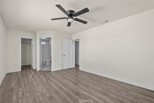 unfurnished bedroom with visible vents, connected bathroom, baseboards, wood finished floors, and a closet