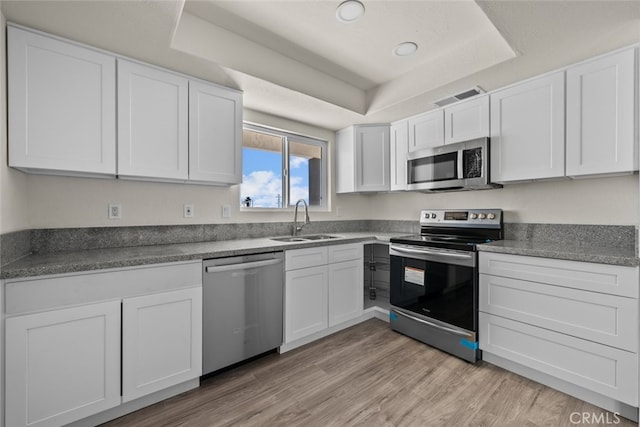 kitchen featuring visible vents, a tray ceiling, appliances with stainless steel finishes, white cabinetry, and a sink