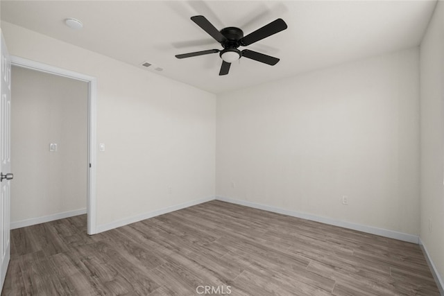 empty room featuring ceiling fan, visible vents, baseboards, and wood finished floors