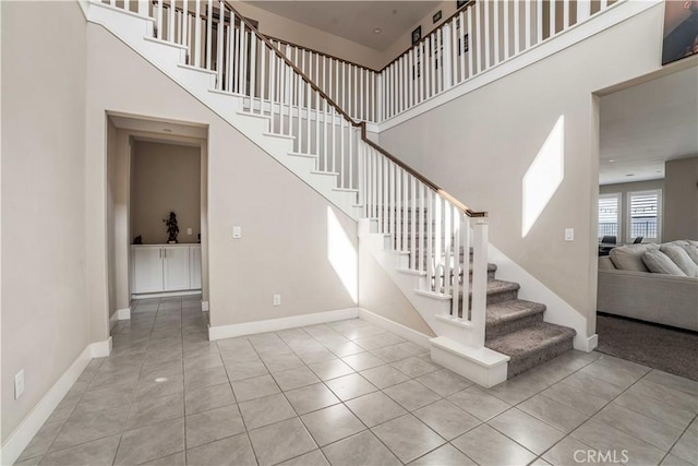 stairs featuring tile patterned floors, baseboards, and a high ceiling