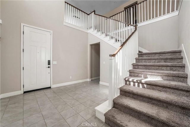 tiled foyer featuring a towering ceiling, stairs, and baseboards