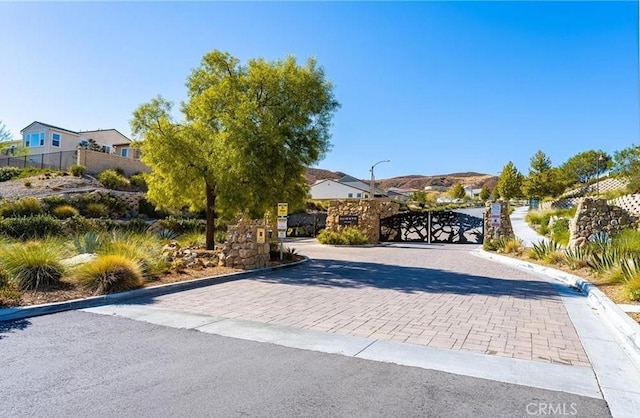 view of street with street lights, a gated entry, curbs, and a gate