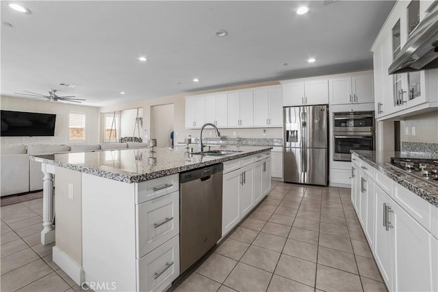 kitchen featuring stainless steel appliances, wall chimney range hood, a sink, light tile patterned flooring, and open floor plan