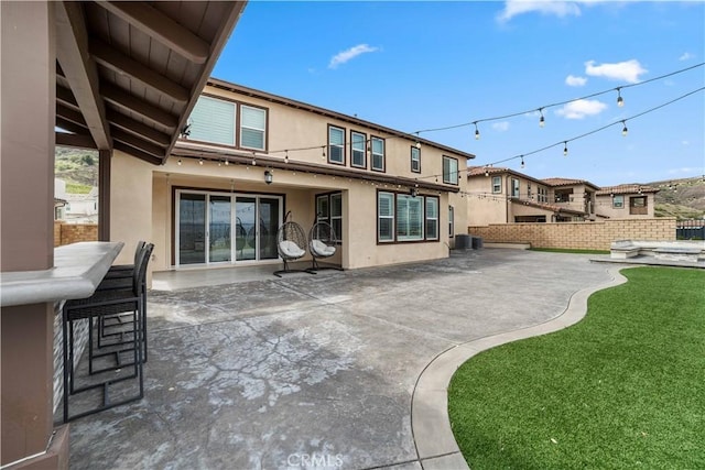 rear view of house featuring outdoor dry bar, central AC, stucco siding, fence private yard, and a patio