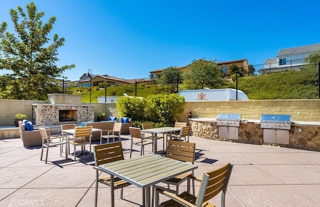 view of patio featuring fence, an outdoor kitchen, an outdoor stone fireplace, and area for grilling